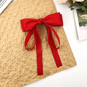 Detail of red satin bow hair clip with long ribbons on a decorative background