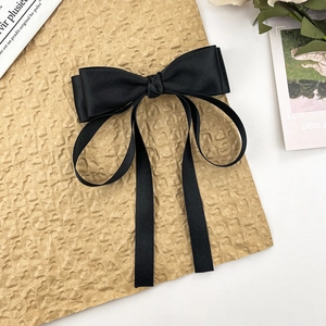 Elegant black satin bow hair clip with long ribbons on vintage decorative background