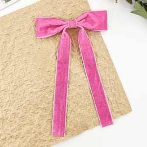Detail of pink velvet bow hair clip with long ribbons on a textured background