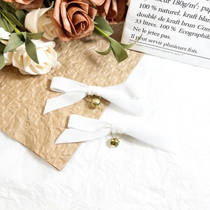 Detailed view of white velvet bow hair clips with golden bells on rustic paper