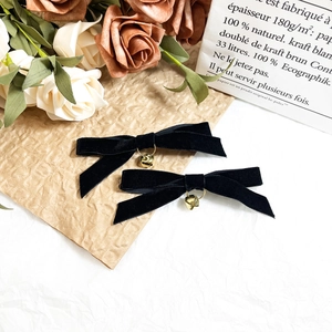 Close-up of black velvet bow hair clips with gold bell charms on rustic floral backdrop