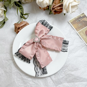 Detail of pink satin bow hair clip with black lace edges and a heart rhinestone center