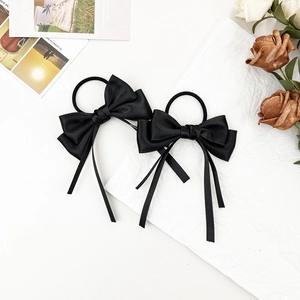 Detail of two black satin bow hair ties with long ribbons on a white artistic background