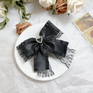 Close-up of elegant black satin bow hair clip with lace trim and heart rhinestone