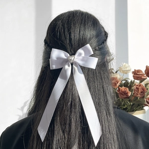 Détail d'un nœud papillon en satin blanc avec strass en cœur et longs rubans sur cheveux