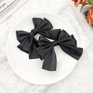 Detail of elegant black satin double-layered bow hair clips on a white lace background