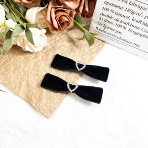 Detail of black velvet bow hair clips with heart shaped rhinestone center and bell