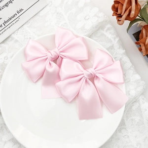 Close-up of two pink satin bow hair clips with elegant silk texture on white lace background