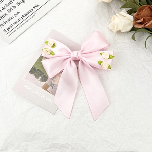 Dettaglio del fiocco per capelli in raso rosa con rose bianche e lunghi nastri eleganti