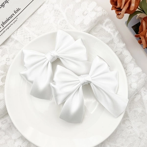 Pair of elegant white satin bow hair clips on a ceramic plate with French lace decor