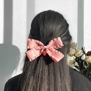 Détail d'une pince à cheveux nœud en satin rose avec bords volantés et pendentif fraise