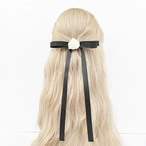 Détail d'un nœud en satin noir avec une rose blanche sur des cheveux blonds bouclés