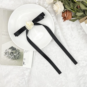 Détail d'un nœud en soie noire avec une rose en tissu crème sur une assiette décorative