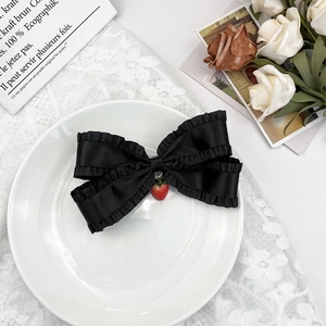Détail d'un nœud papillon en satin noir avec dentelle et petit pendentif fraise rouge