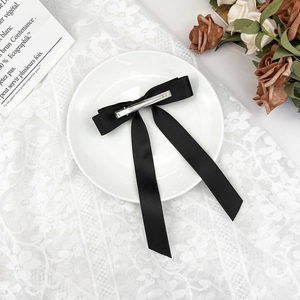 Elegant black satin bow hair clip with long ribbons on a vintage lace background