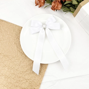 Détail du nœud en satin blanc avec strass cœur et perle sur un plateau élégant