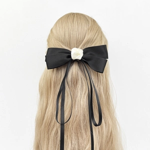 Detail view of a black satin bow hair clip with white rose and long ribbons on blonde hair