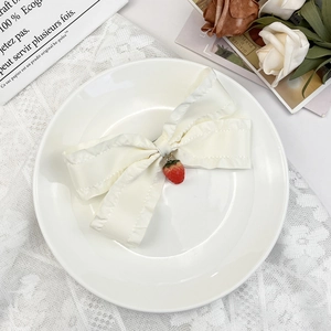 Détail d'une pince à cheveux en satin blanc avec double nœud et pendentif fraise rouge