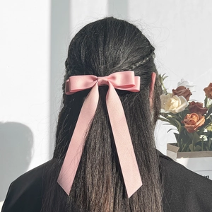 Detail view of pink satin ribbon bow hair clip worn in a half-up hairstyle on a model