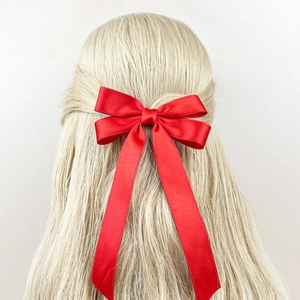 Elegant large red satin bow hair clip with long ribbons on blonde wavy hair