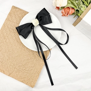 Detailed macro view of black satin bow hair clip with cream rose and long ribbons