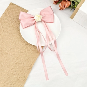 Detailed view of pink satin bow hair clip with creamy rose and long flowing ribbons