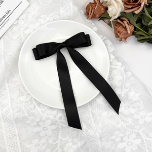 Close-up of elegant black satin bow hair clip with long ribbons on white lace background