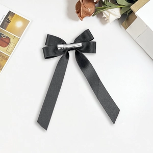 Detail of elegant black satin bow hair clip with long ribbons on white surface
