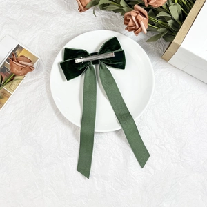 Elegant dark green velvet bow hair clip with long satin ribbons on white ceramic plate