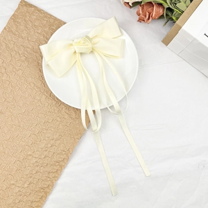 Close-up of cream satin bow hair clip with rose detail and long flowing ribbons