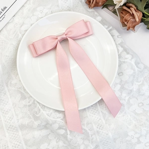 Detail view of pink satin bow hair clip with long streamers on white lace background