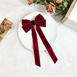 Close-up of deep burgundy velvet bow hair clip with long ribbons on artistic white background