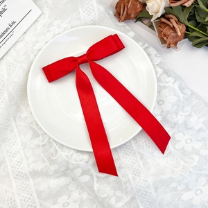 Detail view of a red satin bow hair clip with long ribbons on a decorative plate