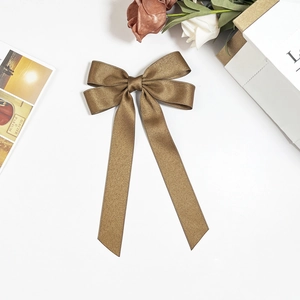 Close-up of elegant bronze satin bow hair clip with long ribbons on white background