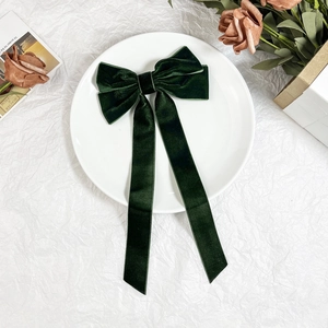 Detail of dark green velvet bow hair clip with elegant long tassels on a white plate