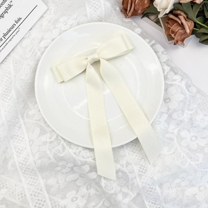 Detailed view of elegant cream satin bow hair clip with long ribbons on a lace tablecloth
