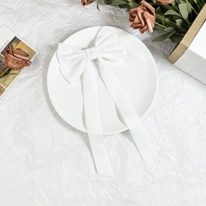 Detailed shot of a white velvet bow hair clip with long ribbons on a ceramic plate