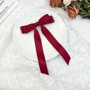 Detailed view of elegant burgundy satin bow hair clip with long ribbons on lace background