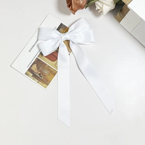 Close-up of elegant white satin bow hair clip with long ribbons and silky texture