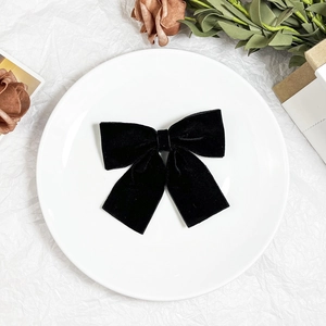 Elegant black velvet bow hair clip with ribbons on white plate and vintage dried flowers