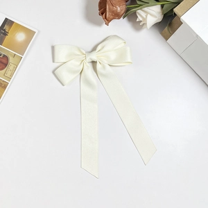 Close-up of elegant cream white satin bow hair clip with long ribbons and silky texture