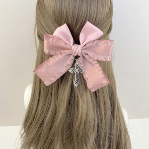 Détail de la barrette à nœud en satin rose avec pendentif croix argentée sur les cheveux