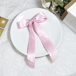 Dettaglio di un fermaglio per capelli con fiocco in raso rosa e nastri su sfondo bianco