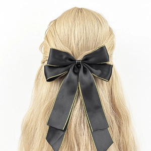 Elegant black satin bow hair clip with gold stitched edges on long blonde hair