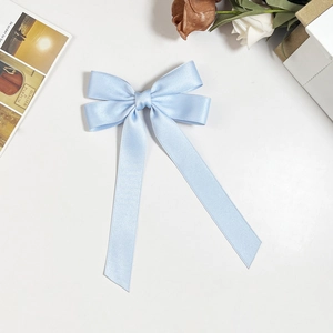 Flat lay of a light blue satin bow hair clip with ribbons on an elegant white surface