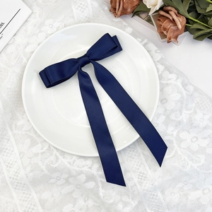 Navy blue satin bow hair clip with long ribbons shown on elegant lace background