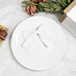 Detailed view of a white velvet bow hair clip placed on a decorative ceramic plate