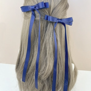 Detail view of dark blue satin bow hair clip with long ribbons on brown wavy hair