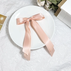 Dettaglio di un elegante fiocco per capelli in raso rosa cipria con lunghi nastri