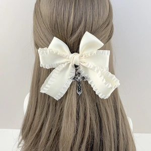 Vue détaillée du nœud en satin crème avec pendentif croix gothique sur cheveux bouclés